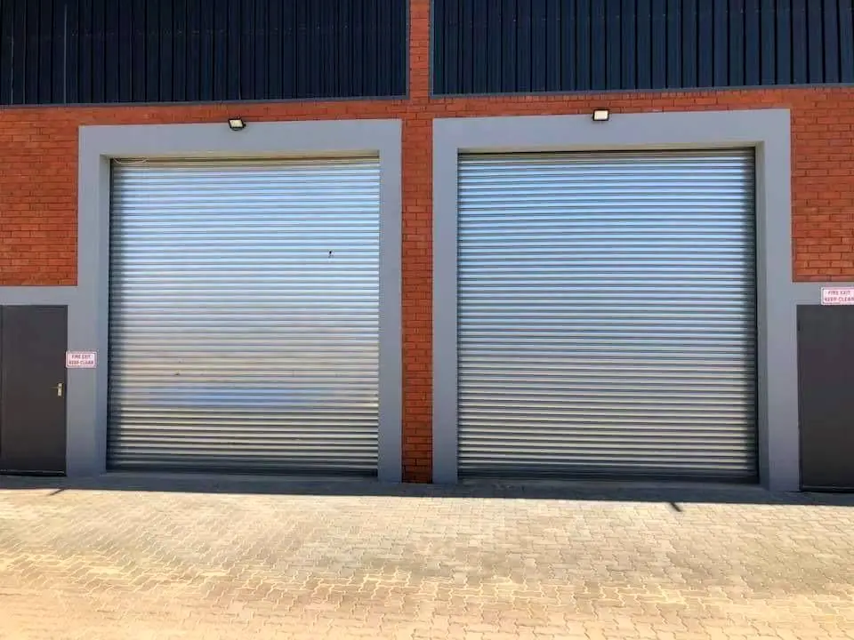 Two galvanised industrial roller doors on a brick and grey-plaster unit